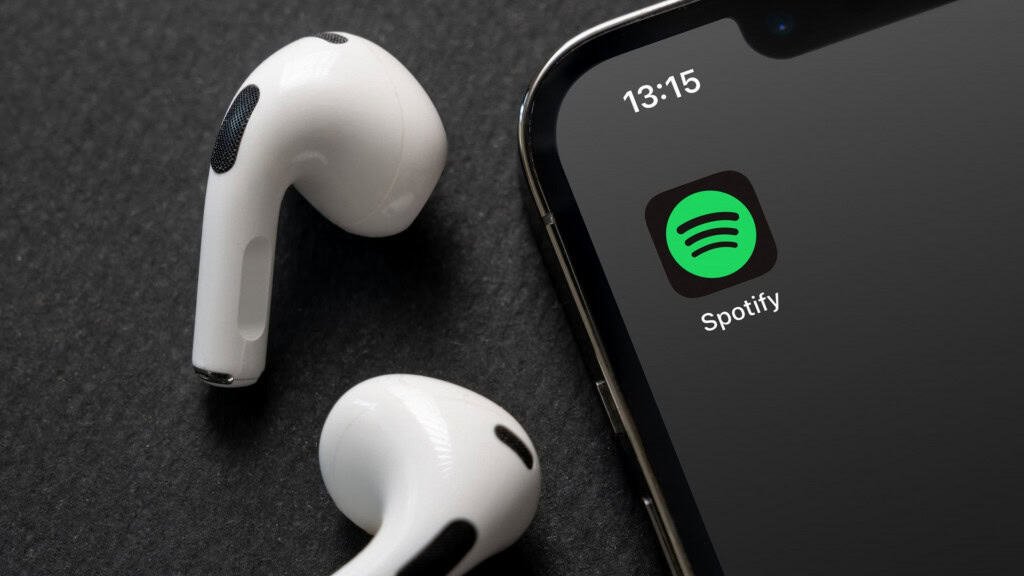 Logo do Spotify em um smartphone, ao lado de um par de fones de ouvido sem fio brancos